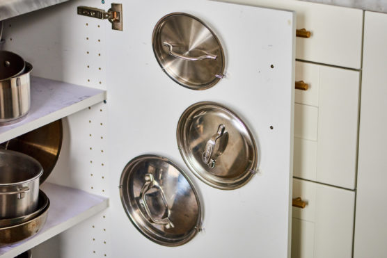 Command hooks attached to cabinet door for pot lid storage